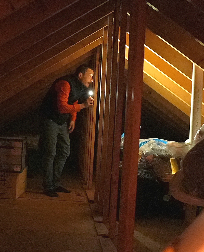a man using a phone as a flashlight looking around in a home's attic