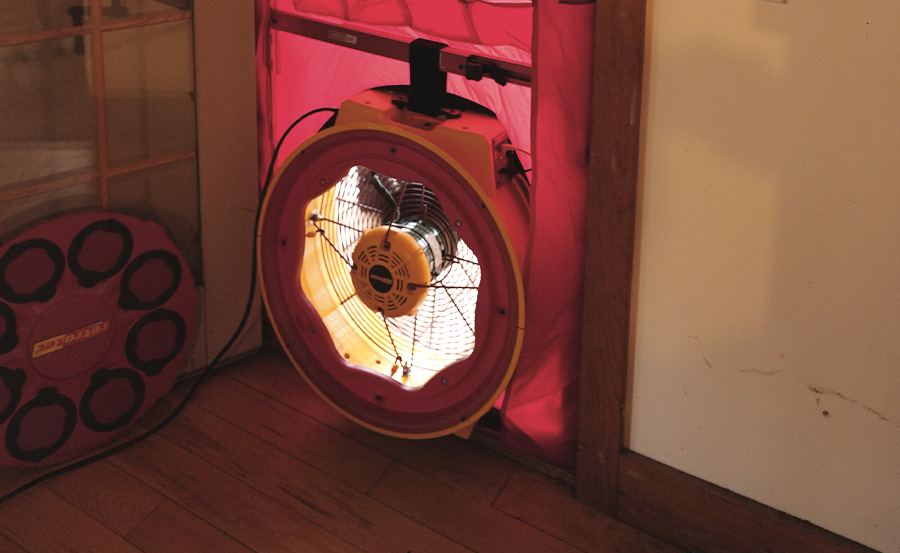 A red blower door set inside an exterior door against a white wall with wooden trim